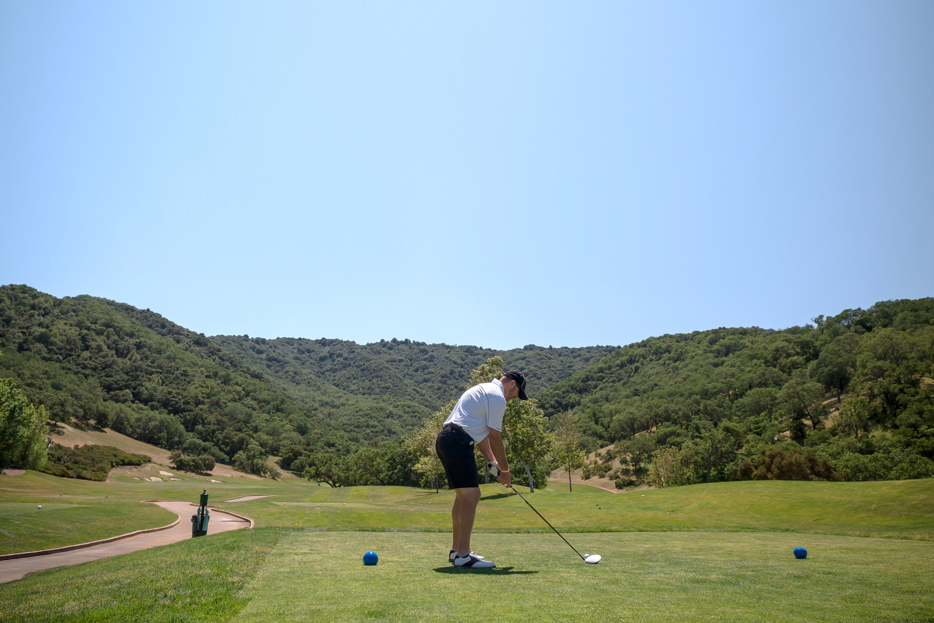 Man in a white shirt and black shorts golfing