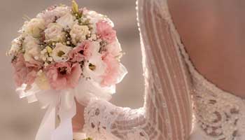Bride wearing a beaded wedding dress and holding a bouquet that has white and pink flowers