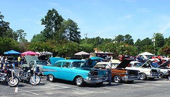 Classic cars with their hoods open and motorcycles in a parking lot