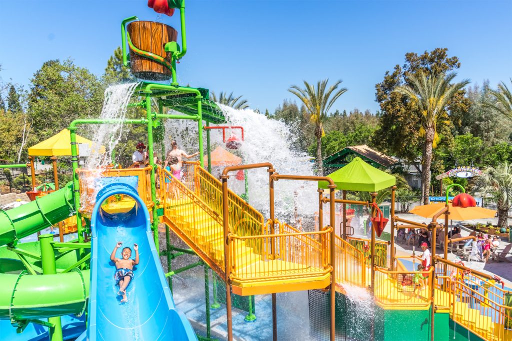 Family in line to go down a blue water slide while a boy is sliding down