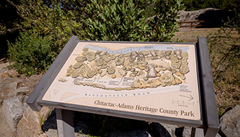 Chitactac-Adams Heritage sign near rocks and green bushes