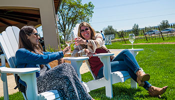 2 women enjoying wine while sitting down outside