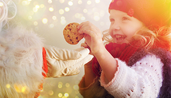 Little girl smiling while grabbing a cookie from Santa Claus
