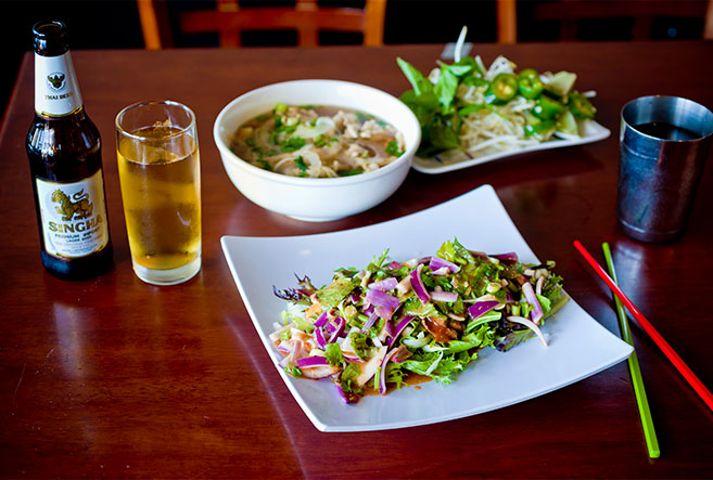 Salad, pho and beer on top of a brown table