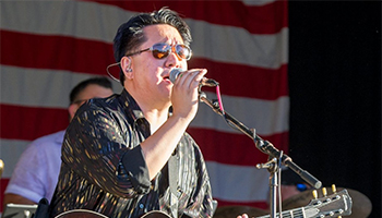 Simon Santiago singing into a microphone with an American flag in the backgroud