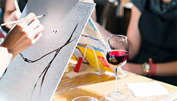 Person painting with a glass of red wine near by