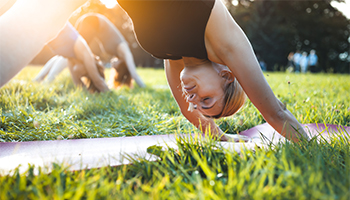Women doing yoga outside on green grass with the bright sun in the background