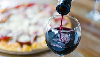 Red wine being poured into a wine glass with a pizza in the background