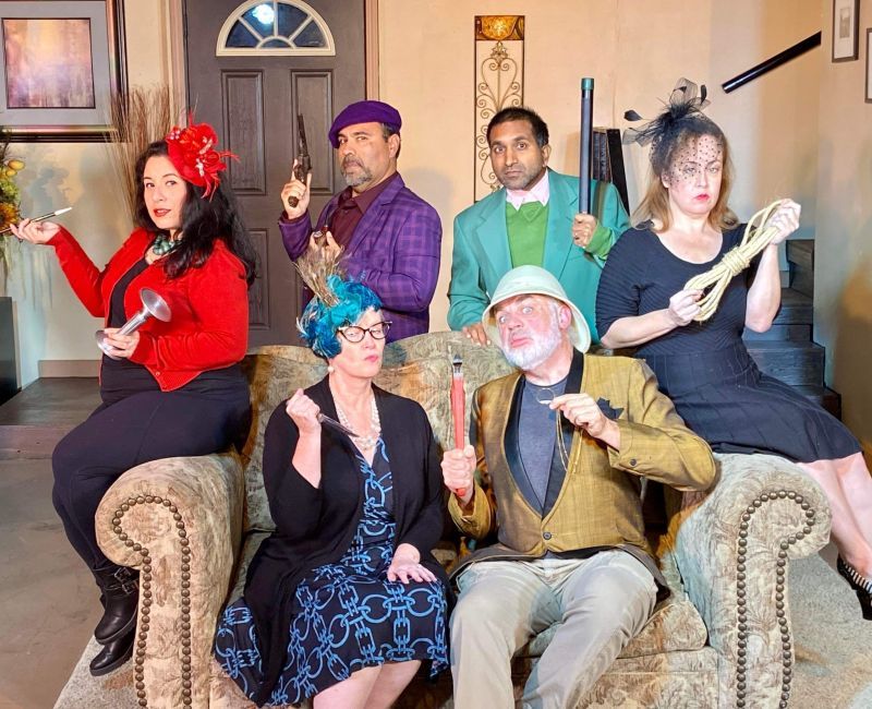 3 Men and 3 Women posing on a sofa with various weapons for the Clue play
