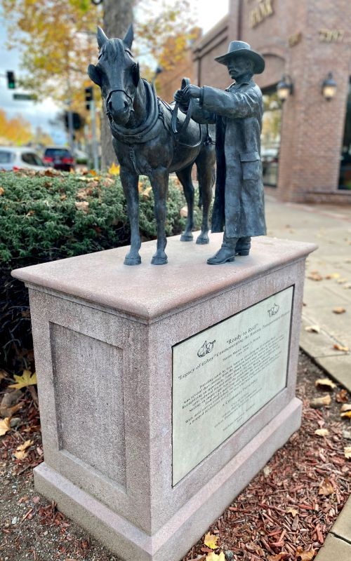 Statue of a station master and a horse on a cement pedestal in downtown Gilroy