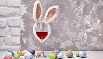 Easter eggs in various colors, blue, green, pink and gold with a glass of red wine with bunny ears