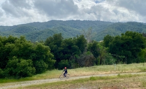 WomanRiding bike with tree-covered hills in background