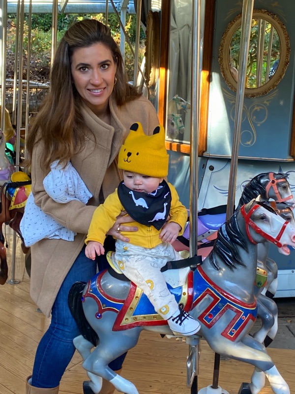 woman with brown hair holding a baby on in yellow hat and clothes on a gray carousel horse