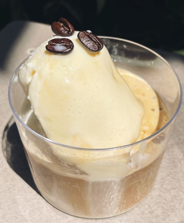 A cup with ice cream with espresso over it and small coffee beans on top