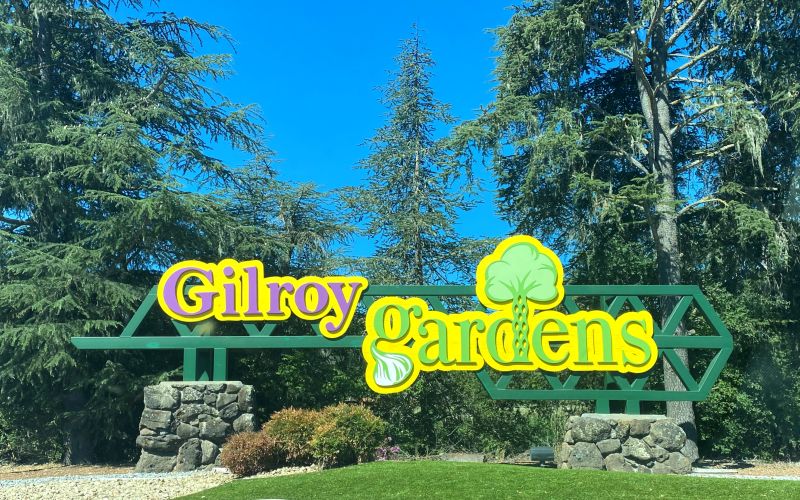 Gilroy Gardens sign with purple and green letters and bright yellow outline in front of the entrance