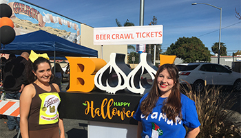 Two women smiling in Halloween costumes near a boo sign