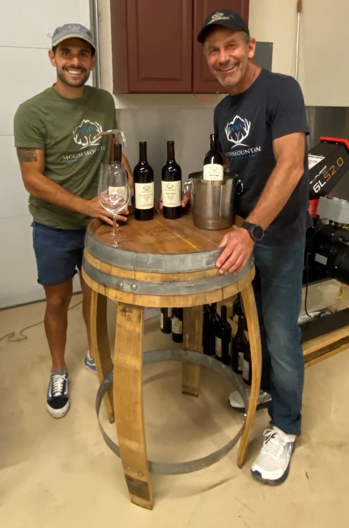 two men with wine bottles and glasses on a wine barrel table