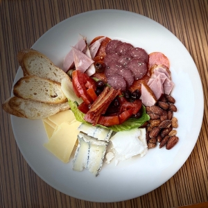 a white plate with meats, cheeses, bread, fruit, and nuts on it