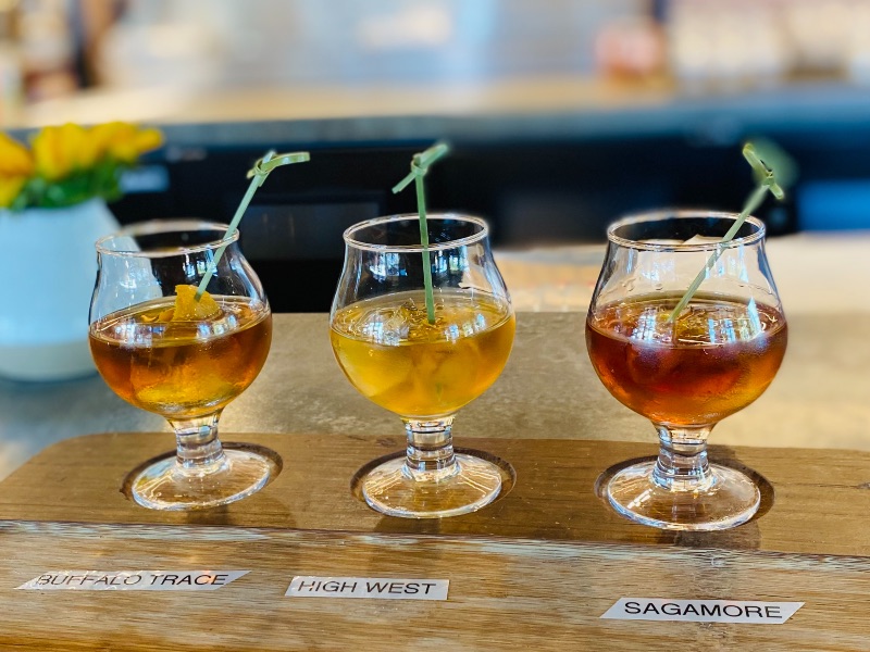three glasses with old fashioned cocktails in the on a wooden serving board
