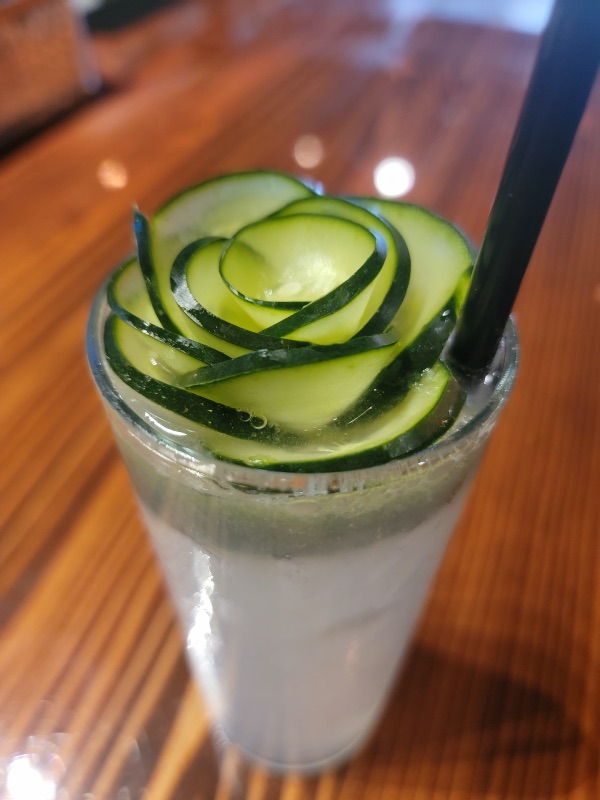 a glass with a cocktail with cucumbers decoratively displayed like a flower on top