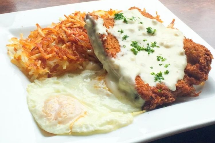 a white plate with a chicken fried steak with gravy, hash browns, and fried eggs