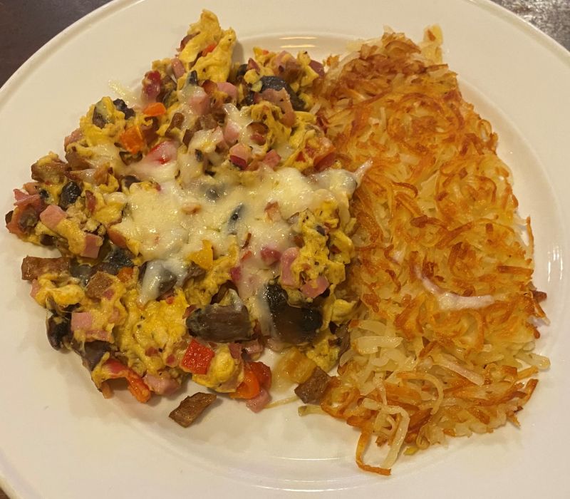 a white plate with hash browns and a bunch of meat mixed in with eggs