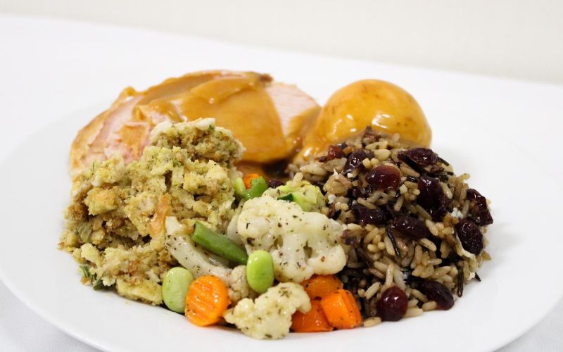 a white plate filled with turkey and mashed potatoes with gravy, stuffing, rice with cranberries, and vegetables