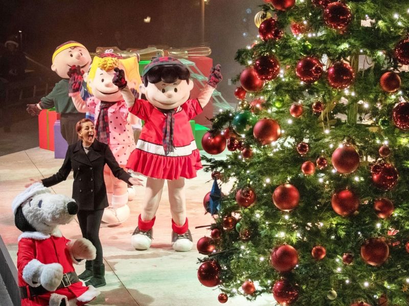 Peanuts characters on stage with a lady singing and a Christmas tree with large red ornaments