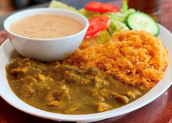 a white plate with chili Verde, some rice, a bowl of refried beans, and a small salad