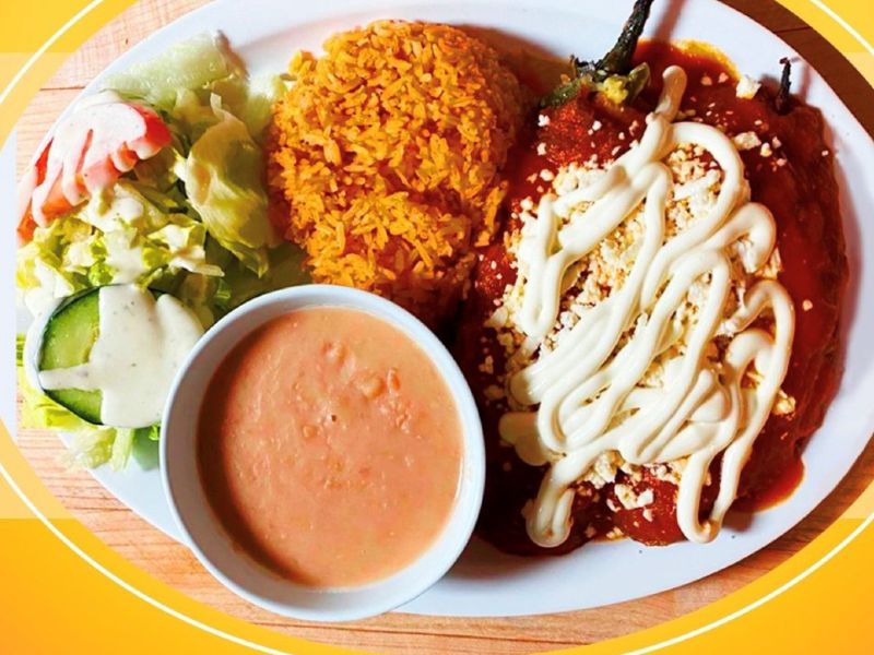 a white plate with peppers covered in sauce and cheese, a scoop or rice, some beans in a bowl, and a small salad