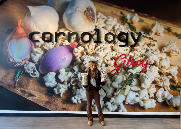 a young woman holds two bags of popcorn with large popcorn wall mural behind her