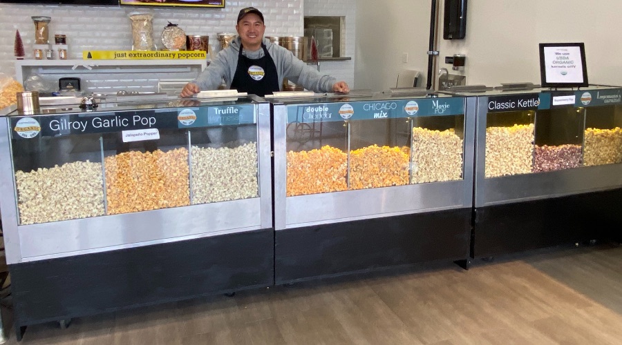 a man smiles behind the counter of a bunch of glass popcorn display cases
