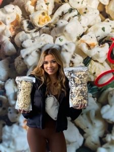 a young woman is holding two bags of popcorn in front of a popcorn mural