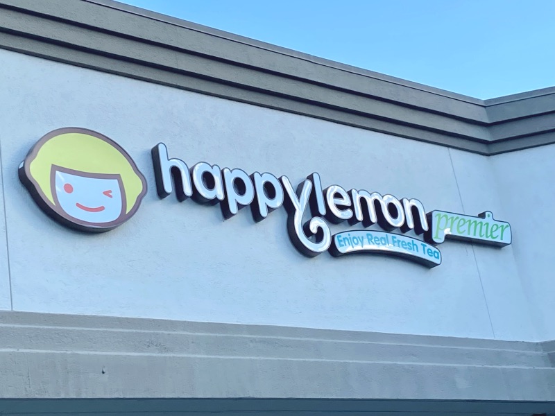 the Happy Lemon logo sign with a lemon character smiling and winking on the outside of their store
