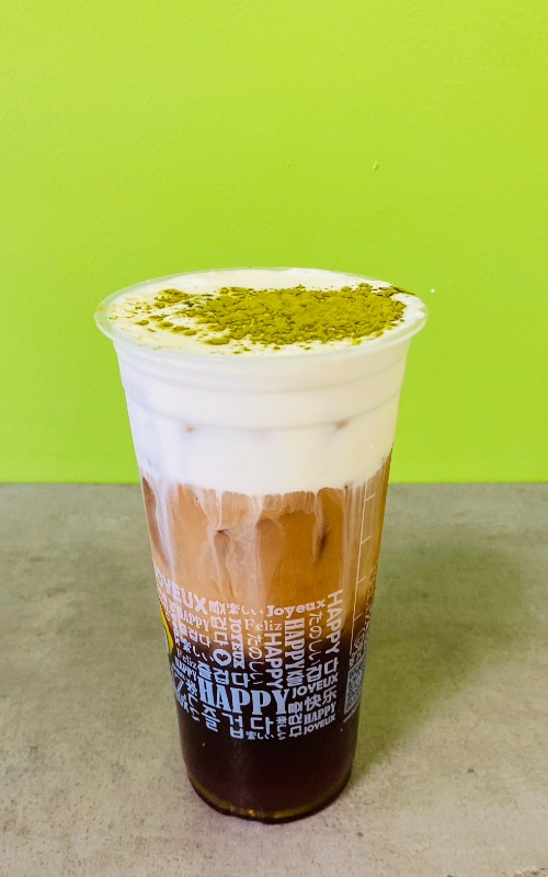 a black tea in a cup with cream on top and green matcha sprinkled on top of the cream with a bright green background