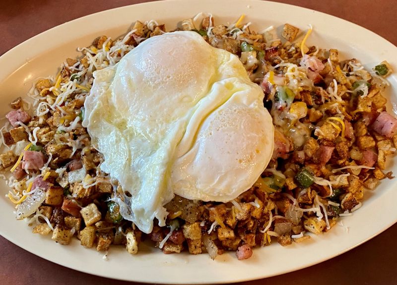 a white plate with diced ham, peppers, onions, and shredded cheese with two fried eggs on top