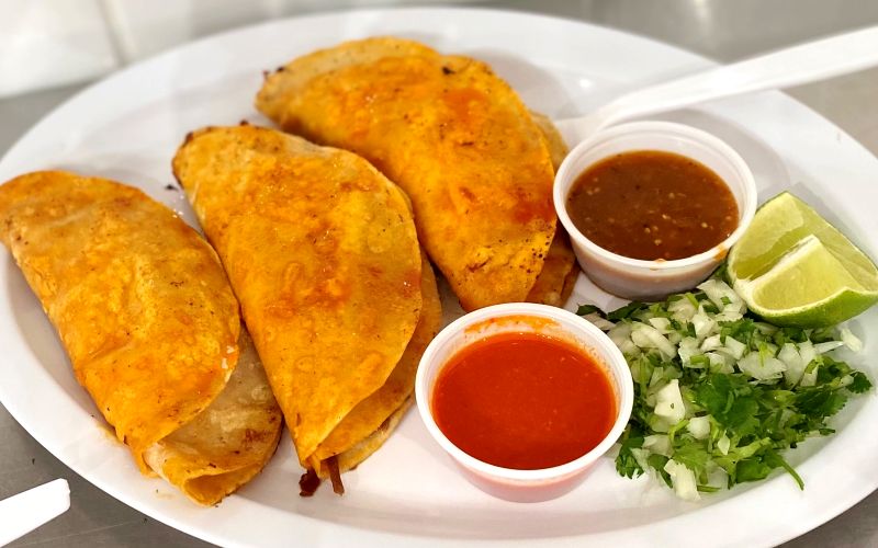 a large white plate with three fried tortillas filled with meat and cheese with salsa on the side