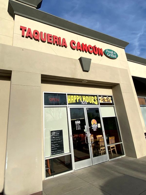 an exterior view of a stucco building and red letters with the name of Taqueria Cancun, a restaurant