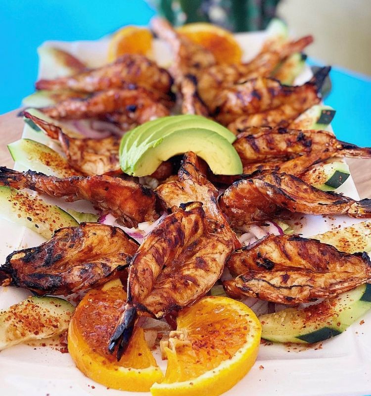 a plate of grilled prawns with oranges and avocado