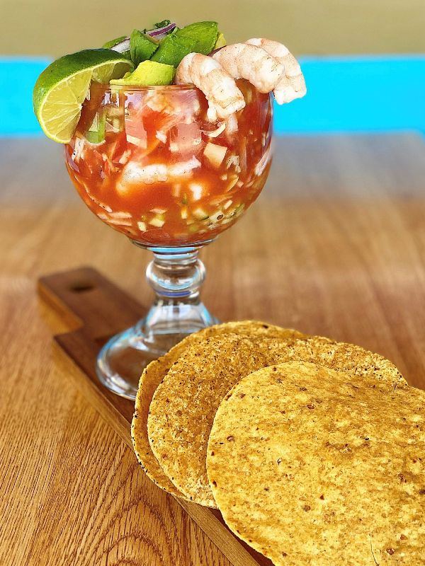 a large cocktail glass of shrimp with limes and tacos on the side