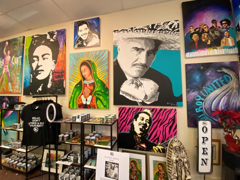 an art gallery wall covered in colorful paintings of different people and some t-shirts and mugs and pictures for sale
