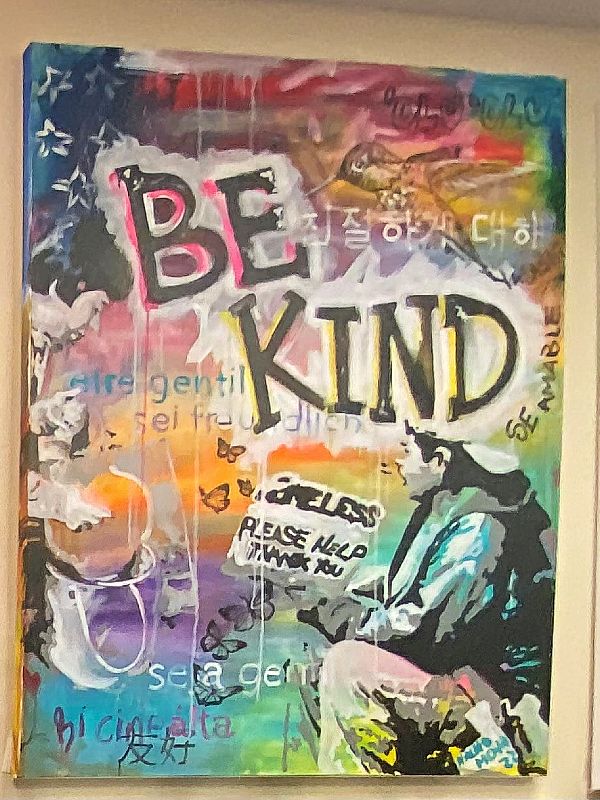 a colorful painting with a man sitting holding a homeless sign and large black letters that say "be kind"