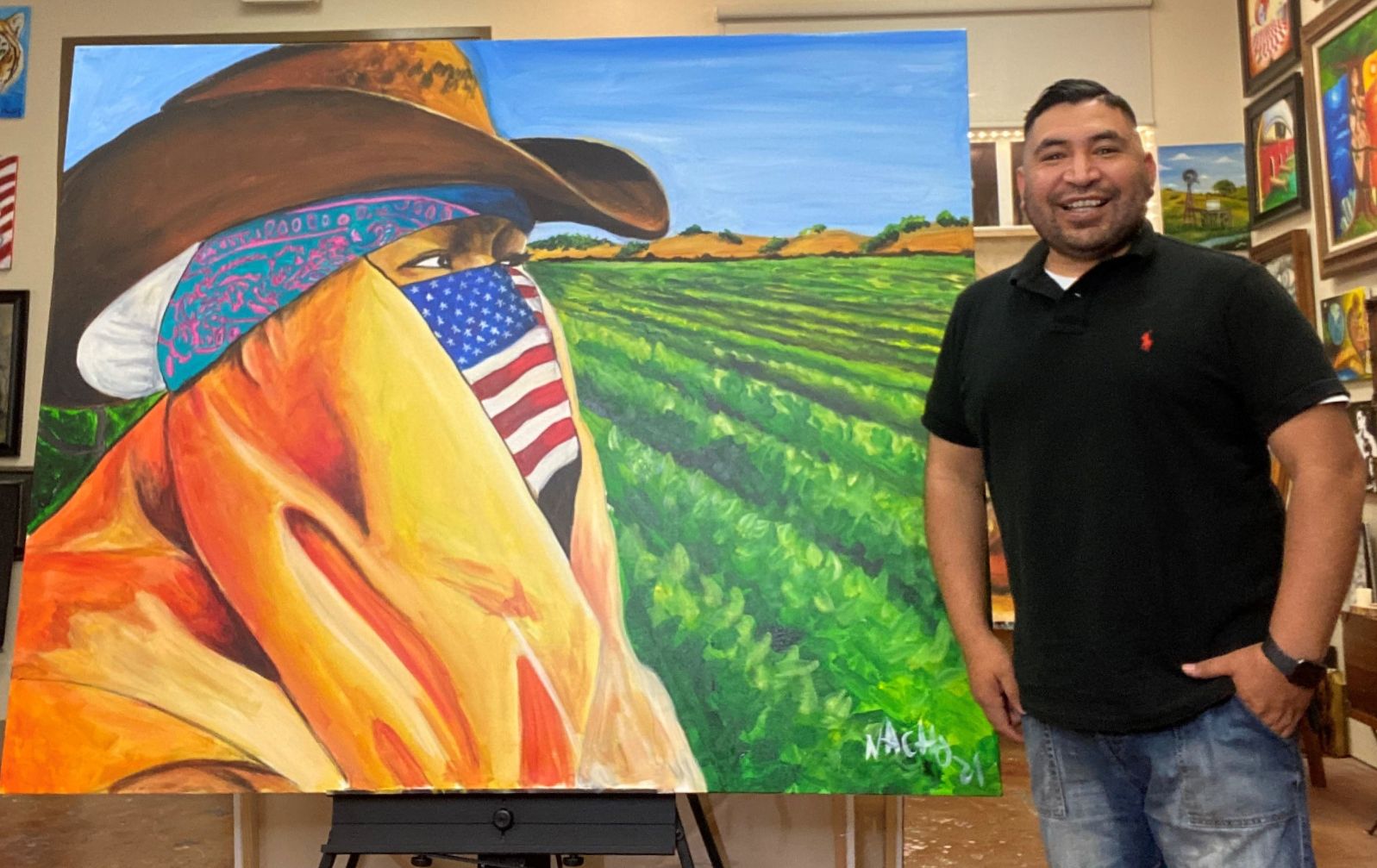 a man in a black shirt and jeans posing by his painting of a farmer in front of a field