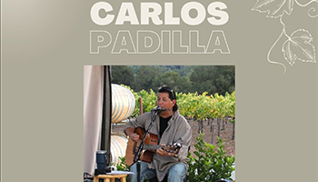 Carlos Padilla playing a brown guitar while sitting on a chair
