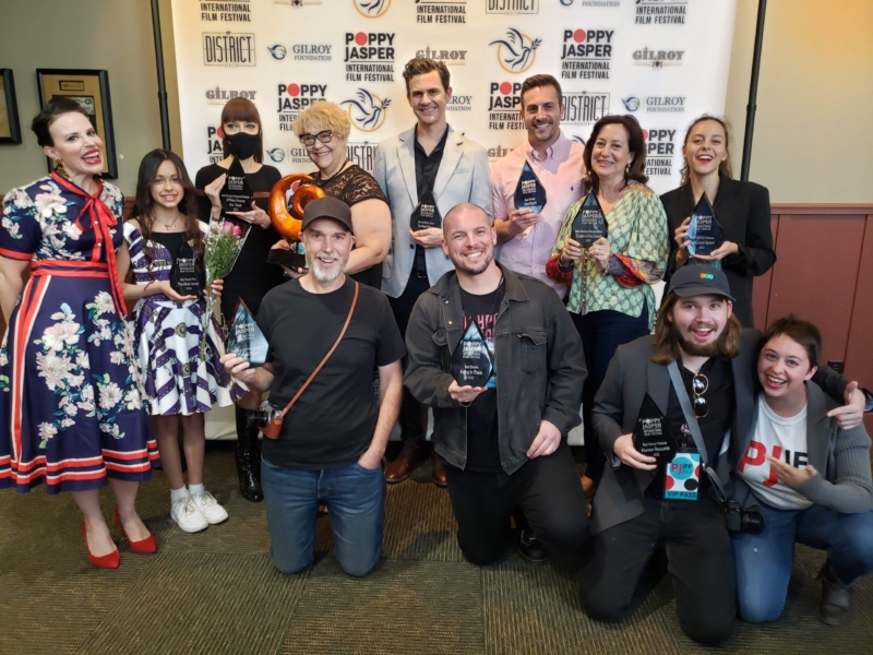 a group of men, women, and a child holding awards in front of a movie background