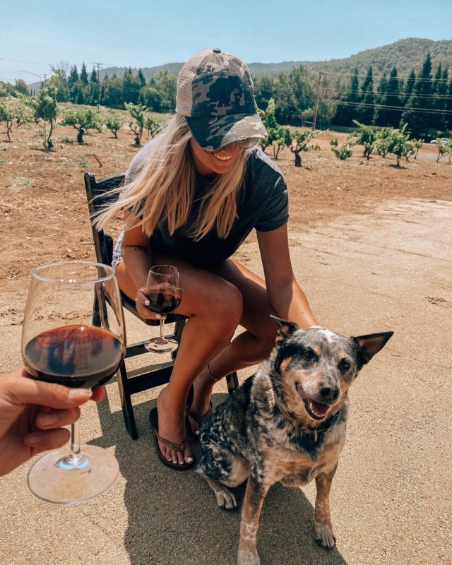 a woman with a wine glass pets a happy dog