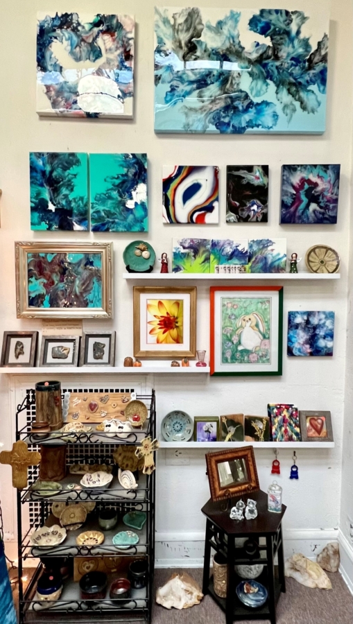 a variety of colorful artwork is displayed on a wall with ceramics on a rack below