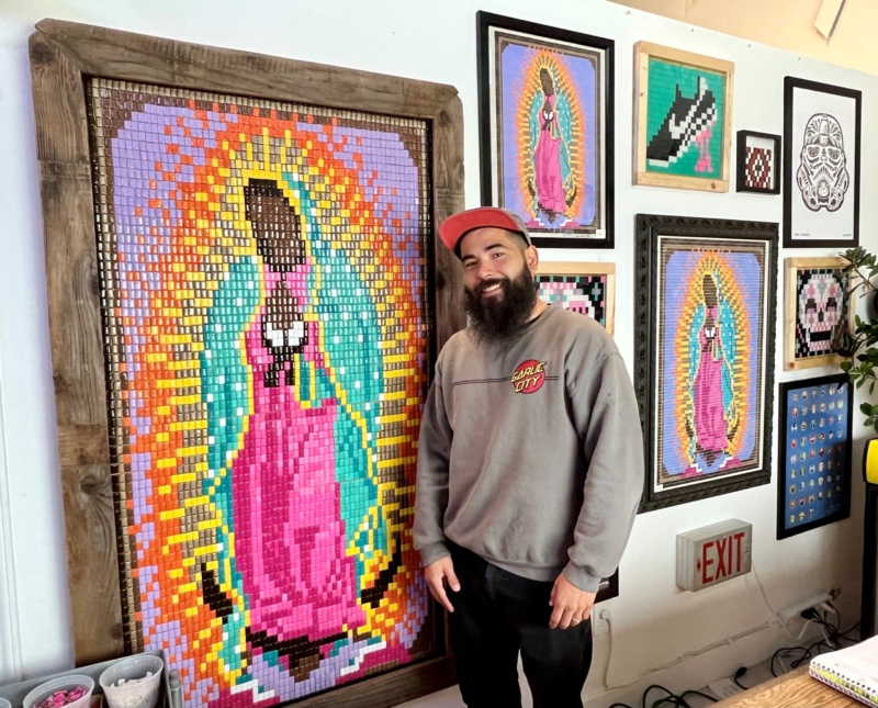 a man smiles next to his colorful artwork mosaics made of Chiclet gum