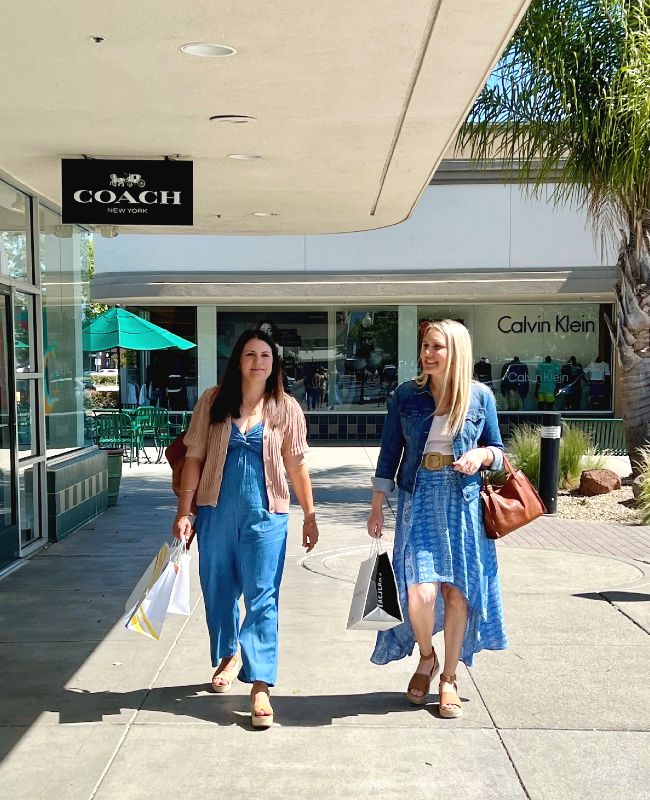 two ladies walking outside some retail stores carrying shopping bags on a sunny day