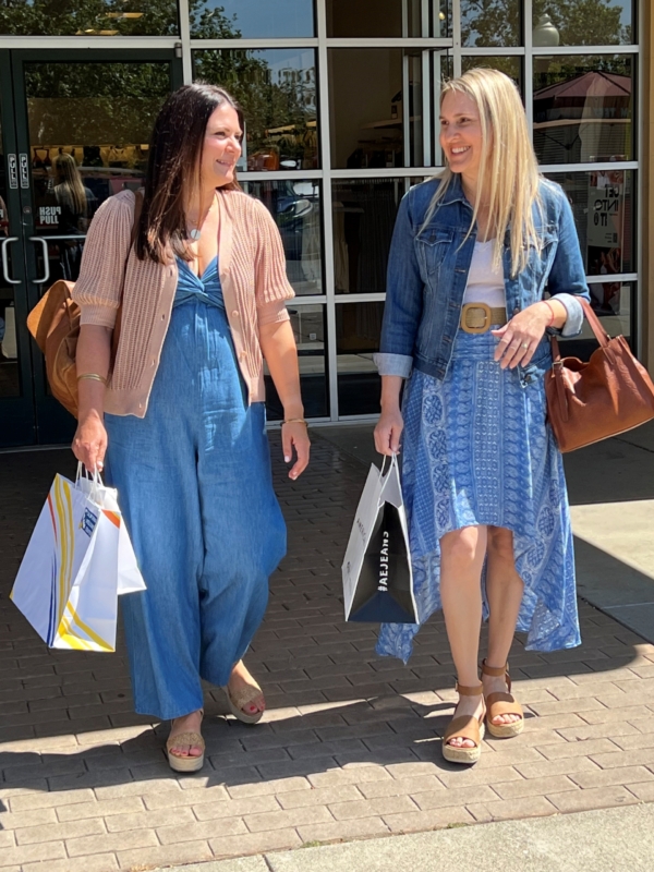 two ladies smiling and carrying shopping bags outside a retail store